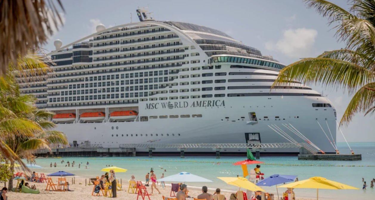 MSC World America docked beside a beach with palm trees